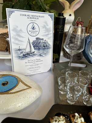 Greek décor flatlay at Cookaki with evil eye charm, olive oil, and menu, Koukáki Athens