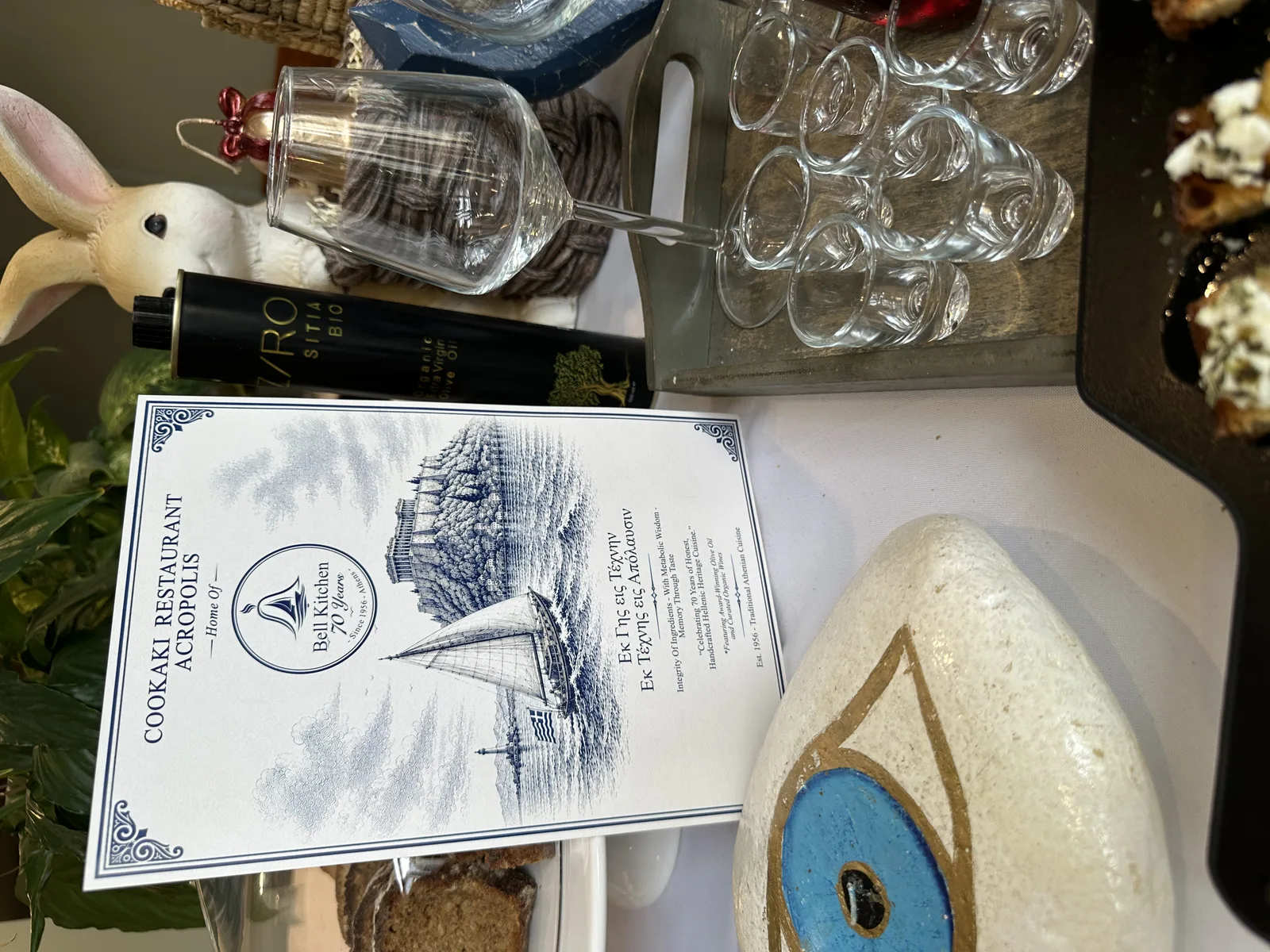 Greek décor flatlay at COOKaki with evil eye charm, olive oil, and menu, Koukáki Athens