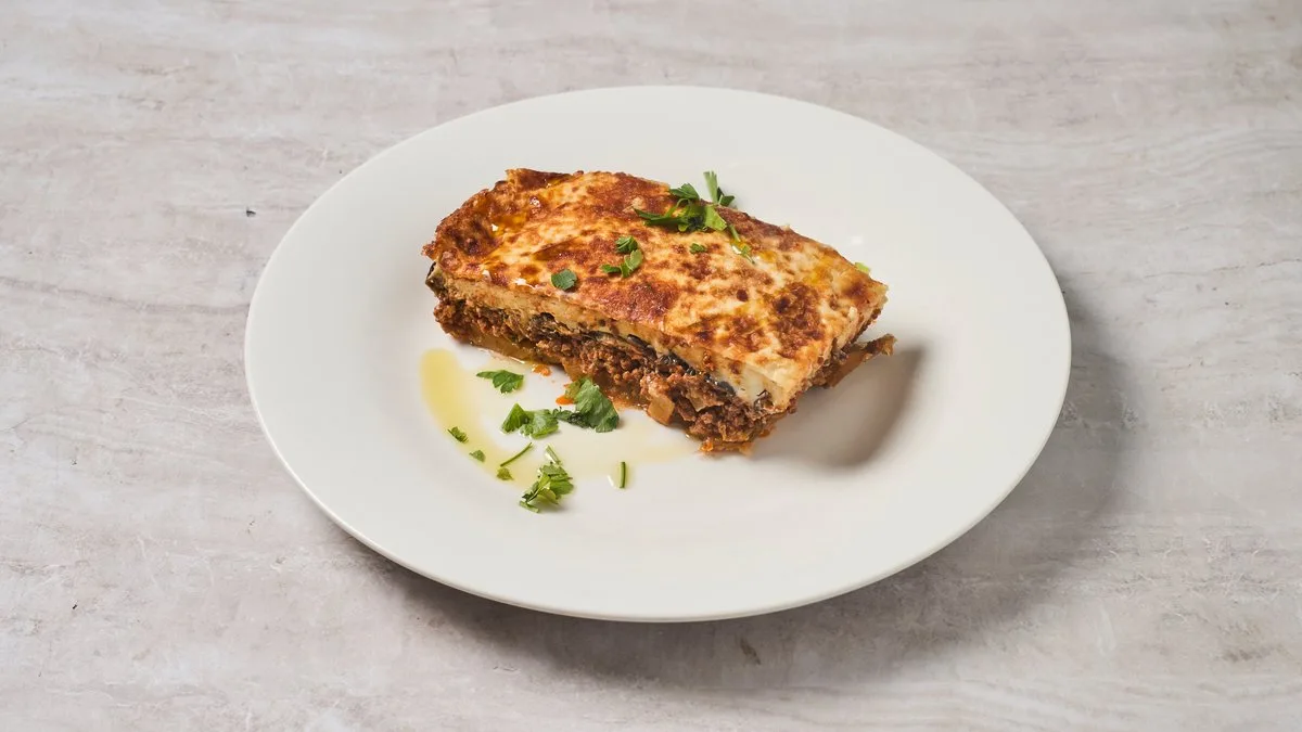 Homemade traditional Greek moussaka with golden béchamel and parsley at Cookaki Athens